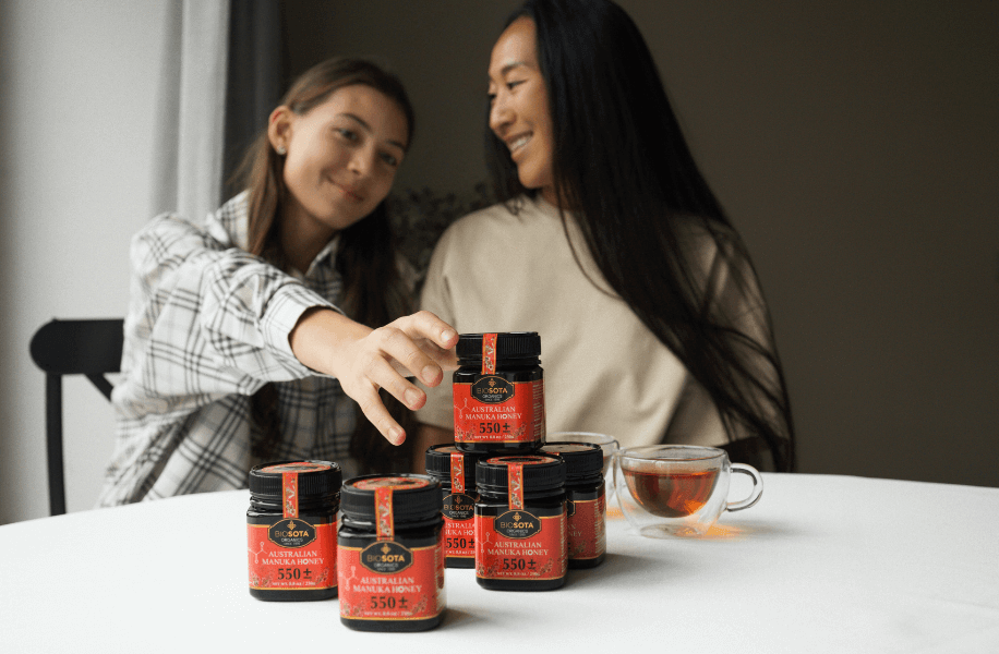 A mother and daughter with jars of Biosota Manuka honey at the table