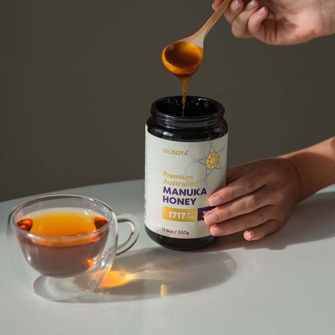 Spooning Biosota Manuka honey from a jar beside a cup of tea